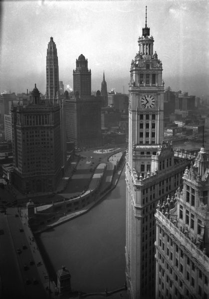 Elevated view of the business district and skyline. The Wrigley Building and clock tower stands in the foreground; it was built in 1920 by William Wrigley Jr. On the opposite bank of the Chicago River stands the London Guarantee Building, featuring a curved central entrance, built by Alfred Schuler in 1922. The 35 East Wacker Drive Building stands to its right, constructed in 1927.
