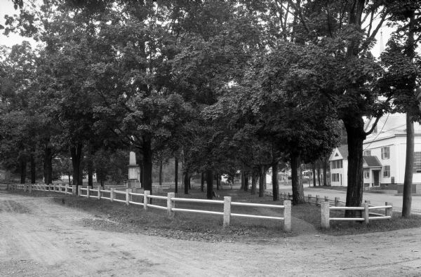 A fence surrounds "The Village Green," a small park with a monument.