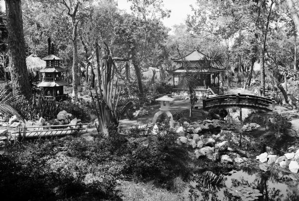 View of the Eagles Nest, a Japanese Garden featuring bridges and a building amongst plants and trees.
