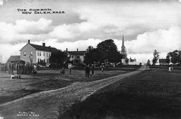 Children play outside New Salem Academy, incorporated in 1795.The steeple of North Congregational Church, built in 1807, is visible beyond the school. Published by Harry W. Fay.