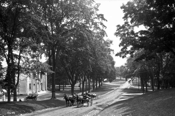 View down residential Main Street.  Horse-drawn carriages and automobiles pass the First Congregational Church, a building with a colonnaded entrance and clock tower built around 1765.