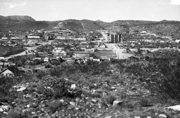 Elevated view of a city located in a hilly landscape. The letter "K" is visible on the hillside.
