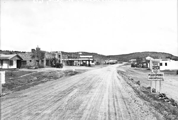 Street scene featuring a gas station and cafe along a dirt road.