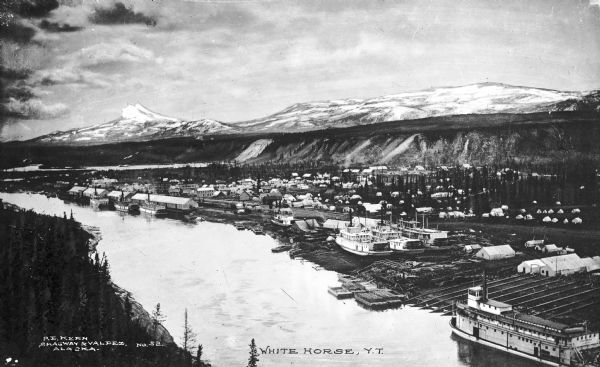 Elevated view of a city along a shoreline. Mountains appear in the background. Published by P.E. Kern, Skagway, & Valdez, Alaska.