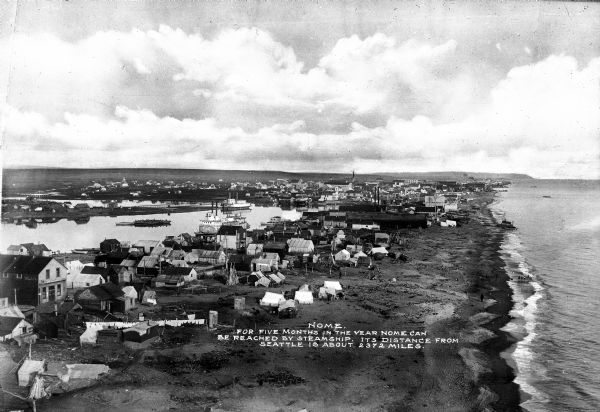 A view of the city at high tide.  Text on the photograph reads, "Nome. For Five Months in the Year Nome Can Be Reached by Steamship.  Its Distance From Seattle Is About 2372 Miles."
