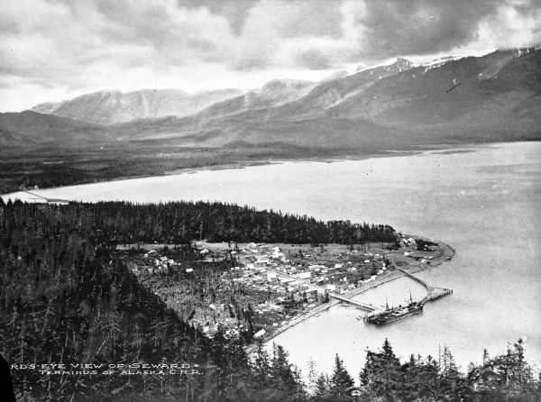 Elevated view of the city and the surrounding bay and hills.  Text reads, "Terminus of Alaska C.R.R."