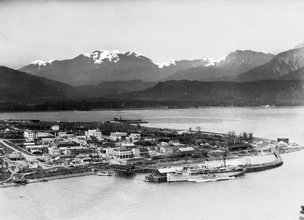 Elevated general view of the city with harbor and mountains.  A ship is docked near the railroad bridge.