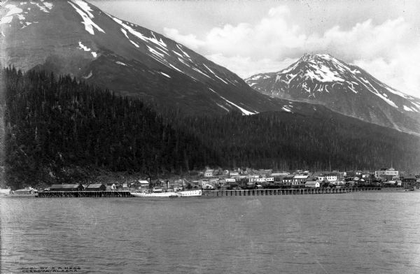 View from the harbor showing the city near the mountainside.  Published by E.A. Hegg, Cordova, Alaska.