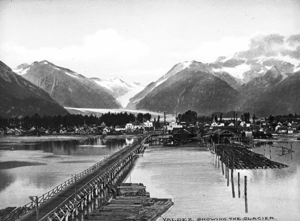 View of the city and glacier as seen from Port Valdez. A pier leads to the city's shore.