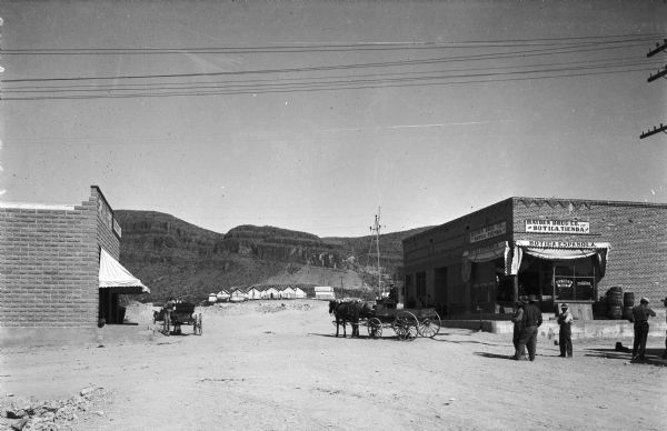 Men walk down a dirt road near horse-drawn carriages and the Hayden Drug Company.