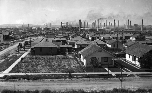 View of a neighborhood with numerous smokestacks in the distance.
