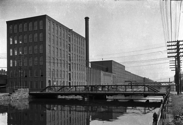 The William Skinner and Sons Silk Mill, founded in 1848, stands along the left bank of a canal. A bridge crosses the water in the foreground.