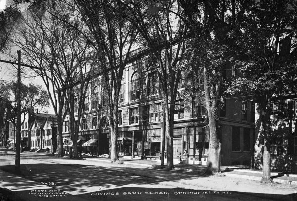 Banks and dwellings stand along one side of the Savings Bank Block. Published by Photo Department of The Old Corner Drug Store.