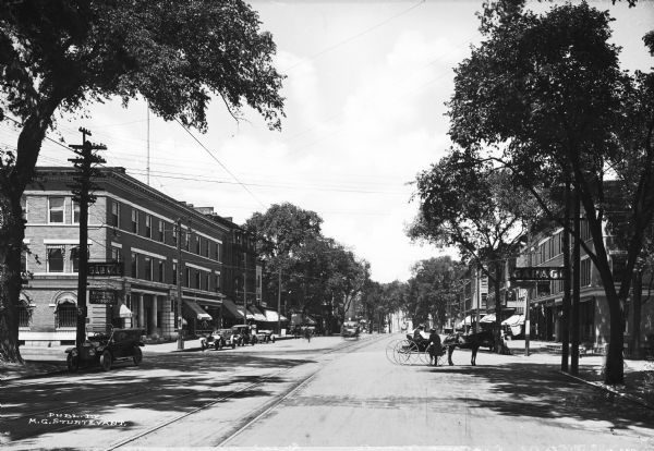 View of Main Street, looking north. A horse and carriage crosses the street near parked automobiles.