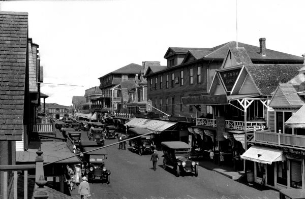 View of the downtown business section crowded with automobiles and pedestrians. A department store on the right is labeled, "Wigwam Block 1900."