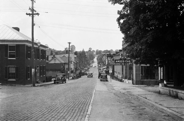 View down Midland Trail.  Automobiles are parked on either side of the street outside an Amoco Station and other stores and dwellings.