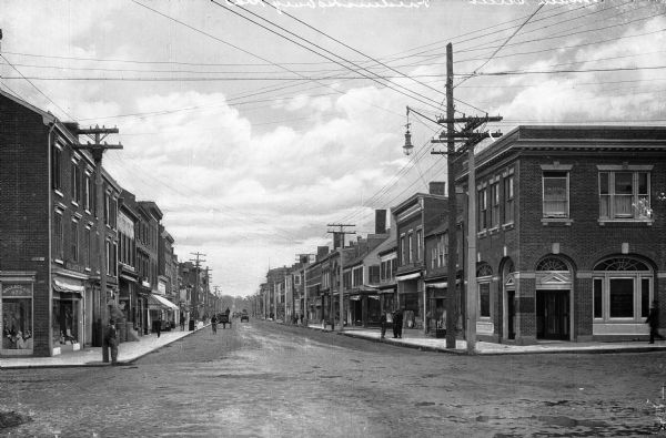 View down Main Street.  Men stand outside stores on either side of the street.