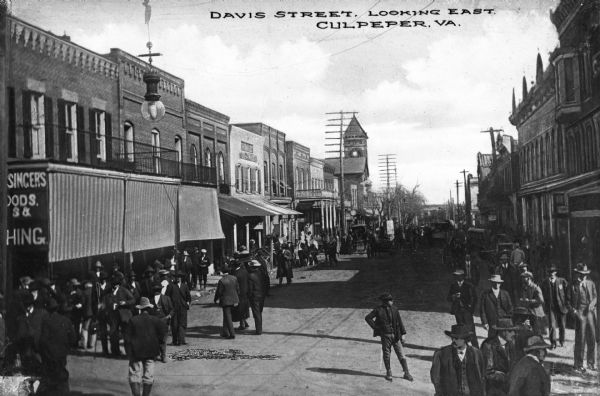 View down Davis Street, a busy downtown area, looking East.  Crowds stand on both sides of the road near storefronts.