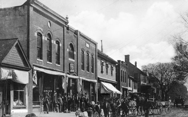 A posed group of townspeople stand outside storefronts on Main Street.