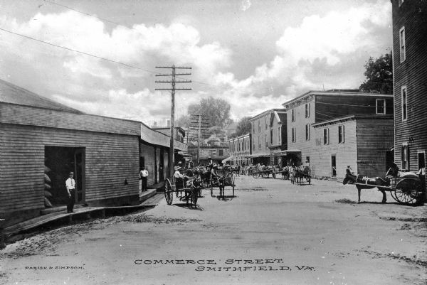 View down Commerce Street featuring several wagons and a warehouse.  Published by Parish & Simpson.