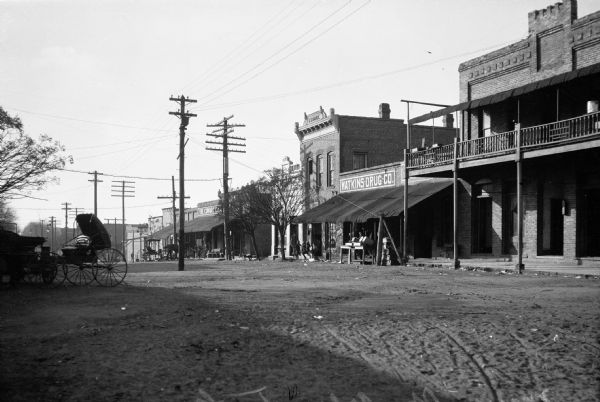 View down unpaved Depot Street.  Men and children can be seen outside Watkins Drug Company.