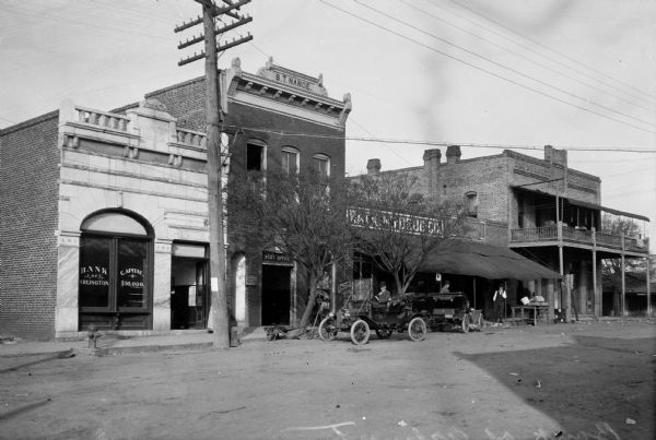 Two cars park in front of the Bank of Arlington and other small businesses. The bank was  built in 1900.