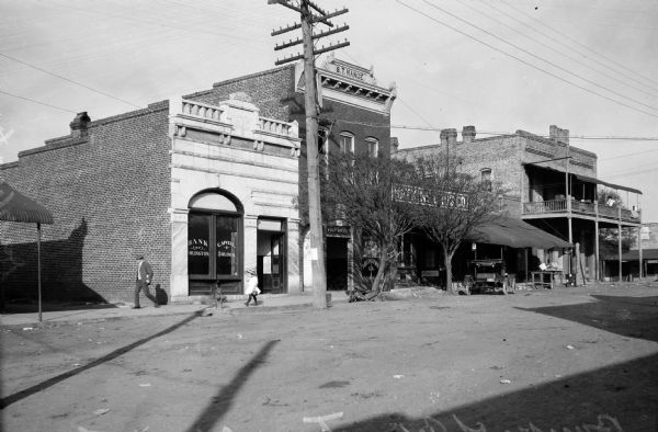 An automobile and pedestrians pass the Bank of Arlington, built in 1900, on Main Street. Other commercial buildings stand nearby.