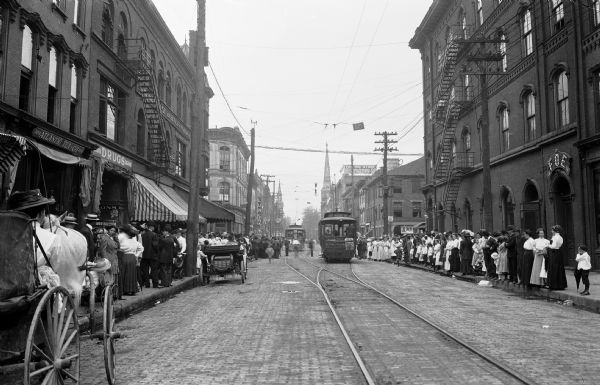 View down a busy street with horse-drawn carriages and trolley cars.