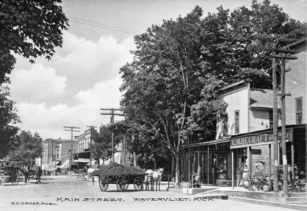 View down Main Street featuring horse-drawn wagons and shops.  Published by G.C. Cross.