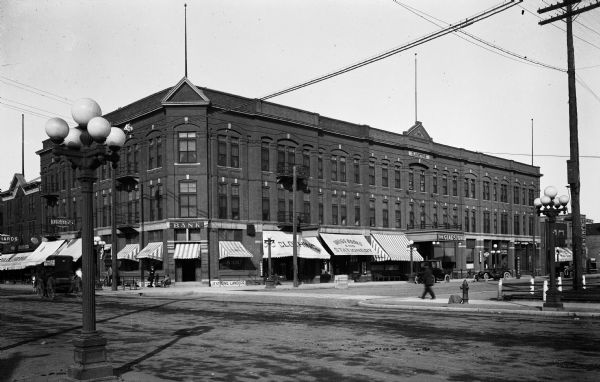 View of a business district intersection with a man perched in the telephone wires overhead.  The Gladstone Hotel, built in 1908, is visible to his right.