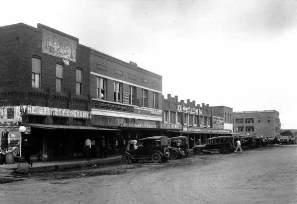 View of storefronts lining a town street.  A brick building housing City Drug Store and Tom W. Crutcher & Co. General Insurance bears a date of 1918.