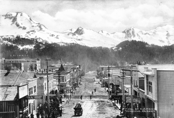 Elevated view of First Avenue, the main street in town. The area is home to the O.K. Lodging House, Denver Bar, and other restaurants and stores. Published by E.A. Hegg.