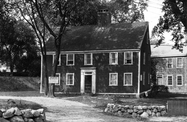 Exterior view of Howland House, a colonial dwelling.  Text on the sign outside the house reads, "Oldest House in Plymouth, Built 1667-Restored 1913, The last house left standing today in Plymouth, whose walls have heard the voices of the Mayflower Pilgrims. Open to Visitors - Admission 25¢."