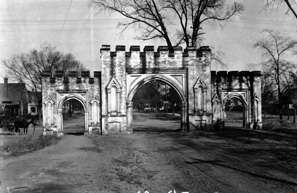 View of a tripartite stone arch over a road.