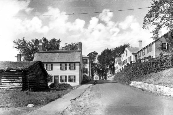 View down a residential street featuring colonial homes and a log cabin.