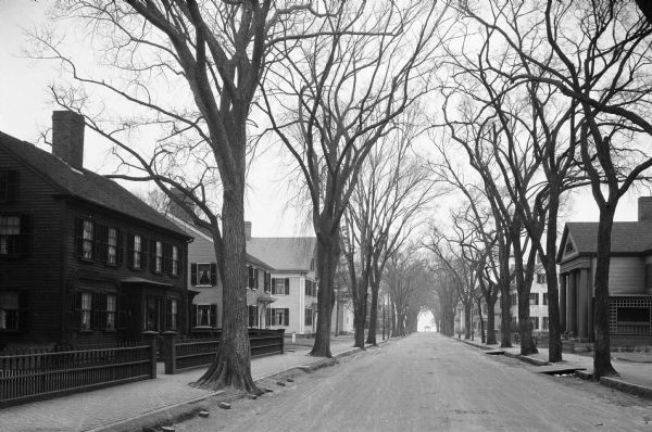 View down a residential street lined with trees.  A colonnaded porch is visible at right.