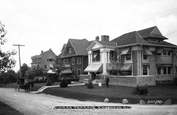 View of Corsa Terrace. A man and young child stand on the lawn outside of one of the homes that line the residential street.