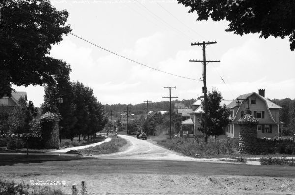 View of the entrance to Kathawood Park, featuring two stone fences on either side of a rural road in a residential area.  E.W. Cobb, Stationer.