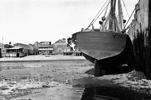 View of a fishing boat, 'Stella,' near a dock and wharf.  The city's shoreline restaurants can be seen in the background.