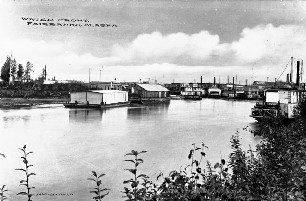 View of the waterfront featuring boathouses, factory buildings, and ships.