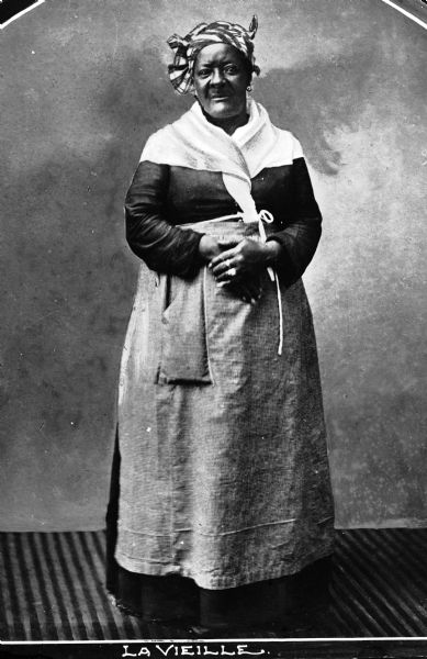 Portrait of a woman wearing a long dress and an apron. Text on photograph reads: "La Vieille."