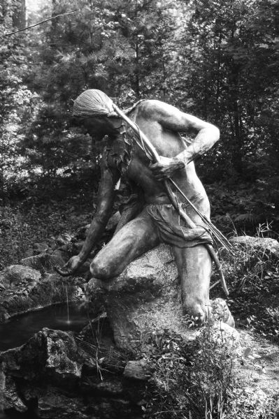 Monument featuring an American Indian sitting on a rock, scooping water with his hand.