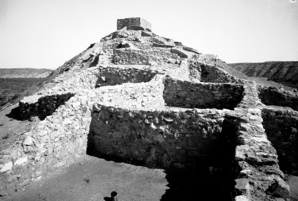 View of Pueblo living quarters, a stone and mortar construction that rises to a central rectangular building.  A sign on the stone walls states, "Keep off the hills."