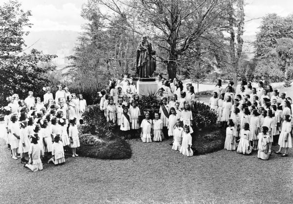 Group portrait of the girls living at Roman Catholic Orphan Asylum, established in 1817 as the Roman Catholic Benevolent Society. The girls gather around a central monument.