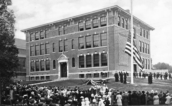 A crowd gathers before a parochial school during a flag-raising ceremony.