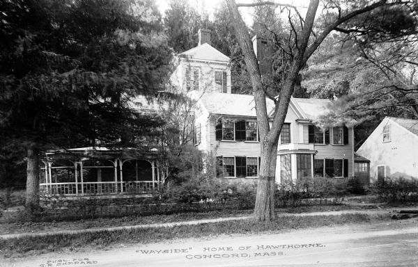 Exterior of Wayside, the residence of Nathaniel Hawthorne, partially obscured by foliage.