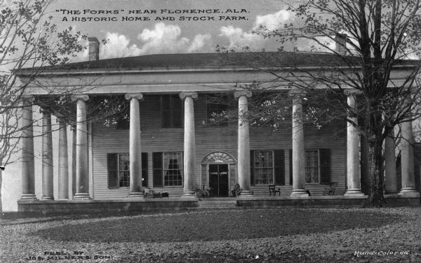 Exterior frontal view of The Forks of Cypress, a Greek Revival style plantation designed by architect William Nichols and completed in 1830.  The main residence features ionic columns which surround all sides of the home.  Published by Joseph Milner & Son.