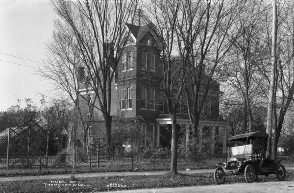 Exterior of the residence of John B. Pinnel, an old gabled home on a residential street. A Ford automobile can be seen parked on the street. Published by Thompson & Co.