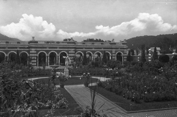 View of the Italian garden at Brookside, the luxurious estate of Mr. W.H. Walker. A fountain and sculpture can be seen amidst the flowers and other plants in the garden, designed by landscape architect Ferruccia Vitale.  Published by M.G. Sturtevant.