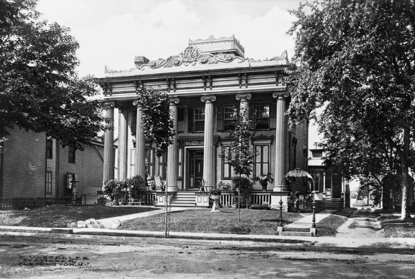 Exterior of the home of the George H. Large family, an elaborate, neo-classical residence featuring an ionic colonnaded porch.  An archway near the sidewalk reads, "George H. Large, Counselor at Law."  Published by E. Vosseller, Stationer.